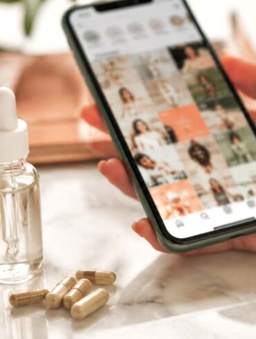 Hand holding phone scrolling wellness content next to peptide supplement vials, illustrating the peptides trend