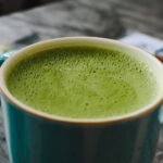 Close-up of a hot matcha latte with frothy green tea in a blue ceramic cup.