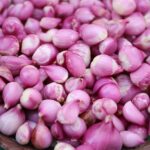 A close-up image of fresh pink shallots piled in a wicker basket.