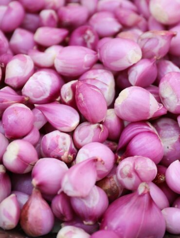 A close-up image of fresh pink shallots piled in a wicker basket.