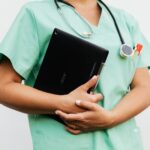 Close-up of a nurse in green scrubs holding a tablet and stethoscope, symbolizing modern healthcare