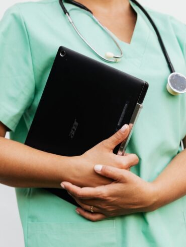Close-up of a nurse in green scrubs holding a tablet and stethoscope, symbolizing modern healthcare
