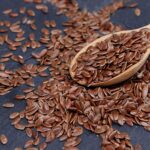 Close-up of brown flax seeds scattered with wooden spoon on slate.