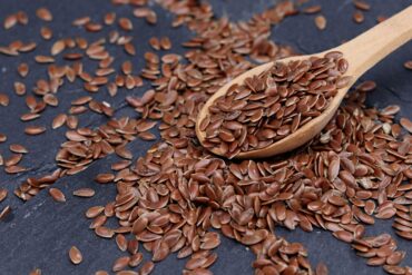 Close-up of brown flax seeds scattered with wooden spoon on slate.
