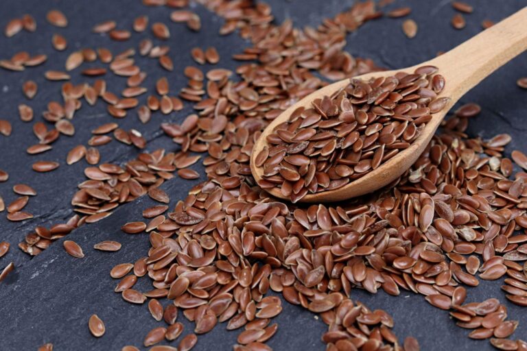 Close-up of brown flax seeds scattered with wooden spoon on slate.