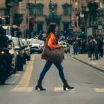 A busy urban street in Rome, Italy, with a young woman crossing among cars and pedestrians.