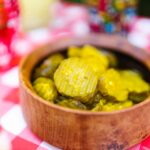 Close-up of pickled cucumbers in a wooden bowl on a red and white checked tablecloth