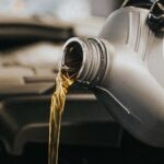 A gloved hand pouring motor oil into an engine. Garage setting.