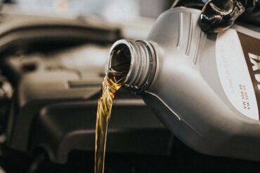 A gloved hand pouring motor oil into an engine. Garage setting.