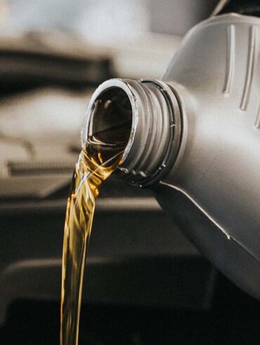 A gloved hand pouring motor oil into an engine. Garage setting.