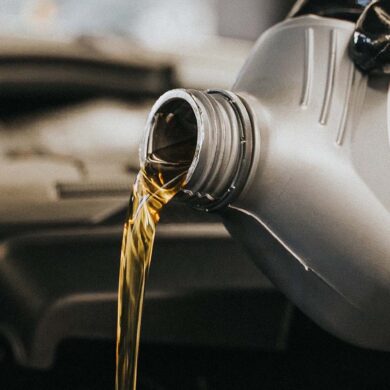 A gloved hand pouring motor oil into an engine. Garage setting.