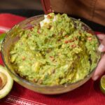 Person preparing fresh guacamole with avocados and limes, showcasing authentic Mexican cuisine