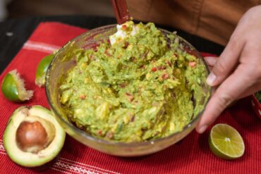 Person preparing fresh guacamole with avocados and limes, showcasing authentic Mexican cuisine