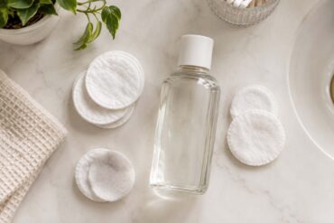 a clear glass bottle of nail polish remover with cotton pads scattered around it on a white bathroom vanity