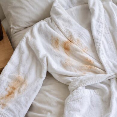 A white cotton robe lying on a bed with orange-brown self-tanner stains across the front and down one sleeve.