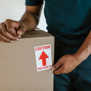 A person handling a moving box with a 'caution this side up' label indoors.