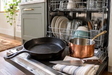 Close-up view of an open dishwasher loaded with dishes, cookware, and other kitchen items, with the dishwasher racks and interior clearly visible.