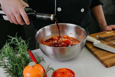 Chef pouring red wine into bowl with herbs and spices for marinade preparation
