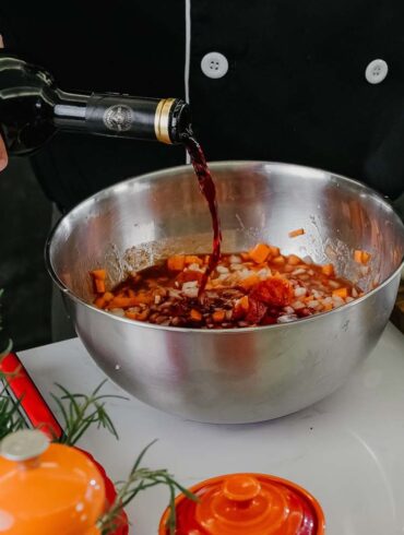 Chef pouring red wine into bowl with herbs and spices for marinade preparation