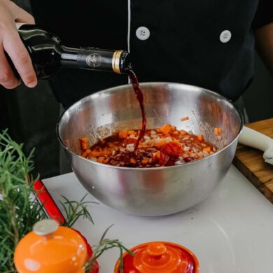 Chef pouring red wine into bowl with herbs and spices for marinade preparation