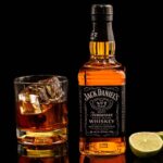 Classic Jack Daniel's whiskey with glass and lime on reflective black surface.