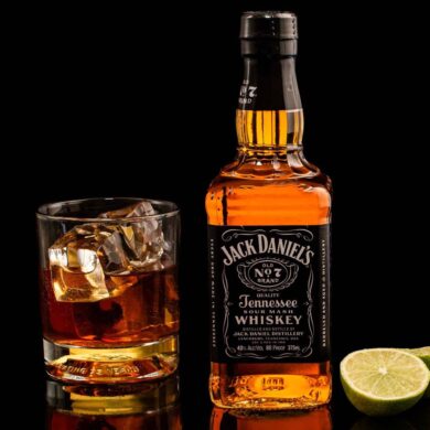 Classic Jack Daniel's whiskey with glass and lime on reflective black surface.