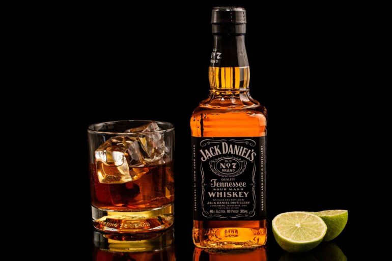Classic Jack Daniel's whiskey with glass and lime on reflective black surface.