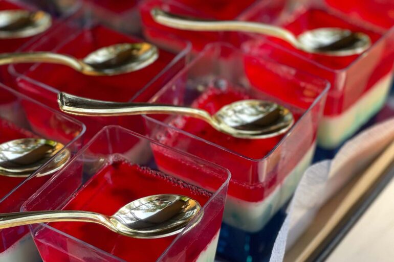 Close-up of colorful layered jello desserts with spoons on a tray