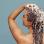 Woman with long hair washing it with shampoo, creating lather, in indoor setting