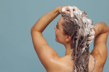 Woman with long hair washing it with shampoo, creating lather, in indoor setting