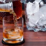 A close-up of whiskey being poured into a glass with ice