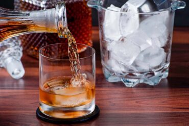 A close-up of whiskey being poured into a glass with ice