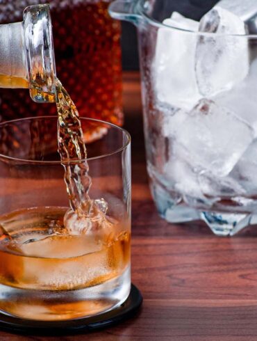 A close-up of whiskey being poured into a glass with ice