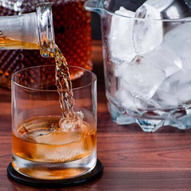 A close-up of whiskey being poured into a glass with ice