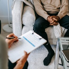 A doctor takes notes as client sits on a sofa during a DNA consultation
