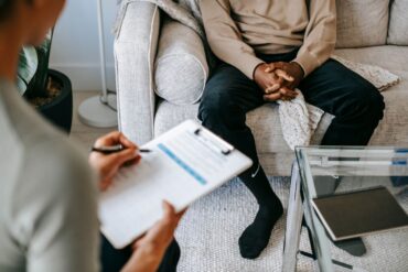 A doctor takes notes as client sits on a sofa during a DNA consultation