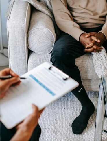 A doctor takes notes as client sits on a sofa during a DNA consultation