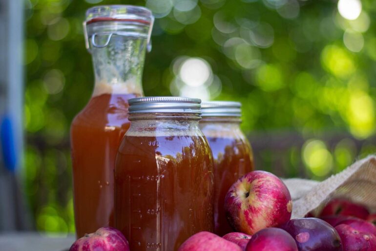 Fresh apple juice in a bottle and mason jars on a table with fresh apples around.