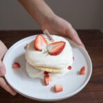 Close-up of a scrumptious strawberry shortcake with Cool Whip on a ceramic plate.