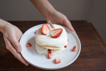 Close-up of a scrumptious strawberry shortcake with Cool Whip on a ceramic plate.