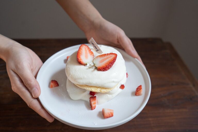 Close-up of a scrumptious strawberry shortcake with Cool Whip on a ceramic plate.