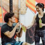 A man and woman sharing Gatorade in an energetic gym setting.