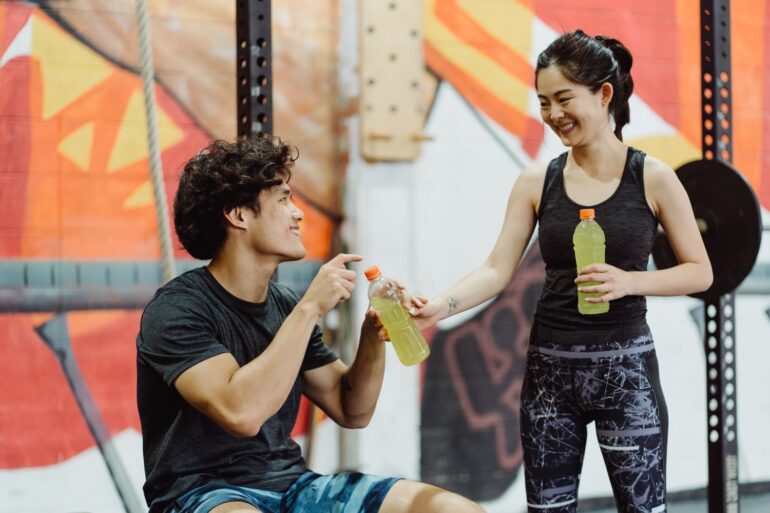 A man and woman sharing Gatorade in an energetic gym setting.