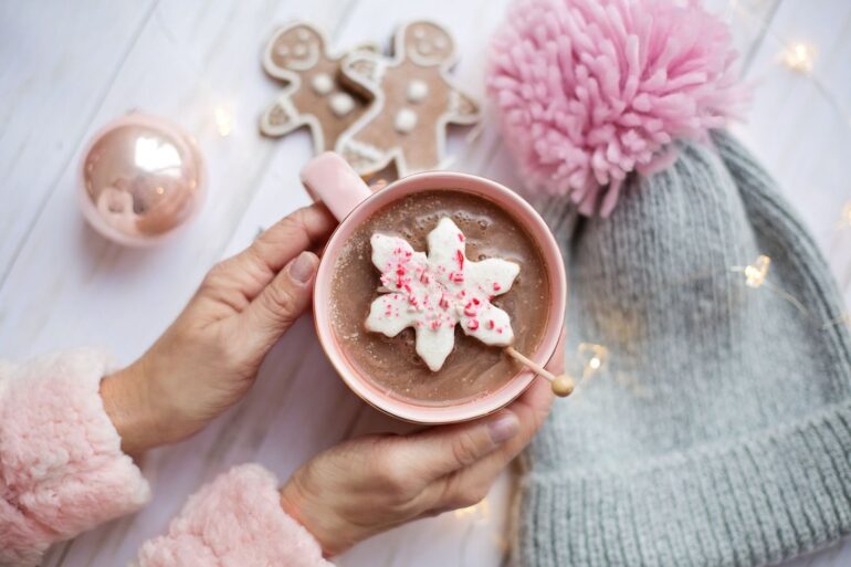 Warm holiday scene featuring hot chocolate with a festive snowflake marshmallow, beanie, and gingerbread.