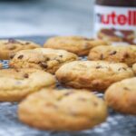 Close-up of homemade chocolate chip cookies cooling with a jar of Nutella in the background.