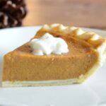 Close up of a slice of cut pumpkin pie on a plate with a dollop of whipped cream.