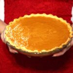 A woman in a holiday dress holding a fresh baked pumpkin pie