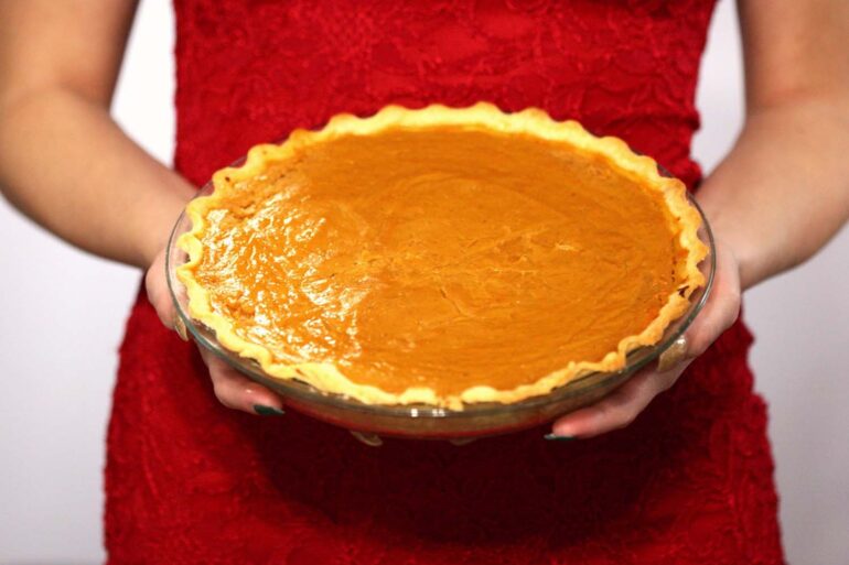 A woman in a holiday dress holding a fresh baked pumpkin pie