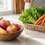 two distinct groups of fresh produce intentionally separated from each other. In the foreground, several ripe red and pink apples and one ripe yellow banana sit naturally together in a simple shallow wooden bowl. A short distance away, a loose arrangement of crisp leafy green lettuce, fresh carrots with natural tops, and a few firm cucumbers sits in a separate open produce basket