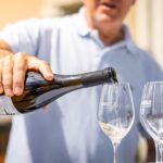 Adult pouring white wine into a glass outdoors at a wine tasting event.